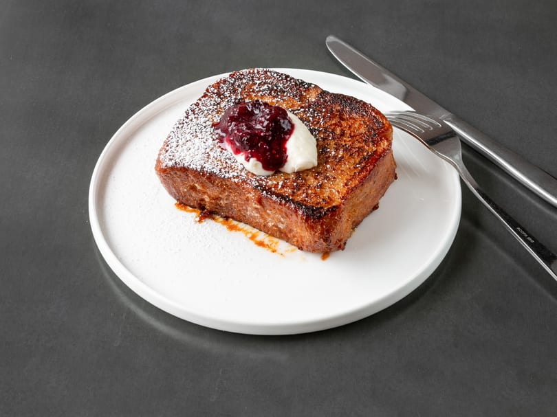Thick-cut French toast with powdered sugar, berry compote, and whipped cream on a white plate.
